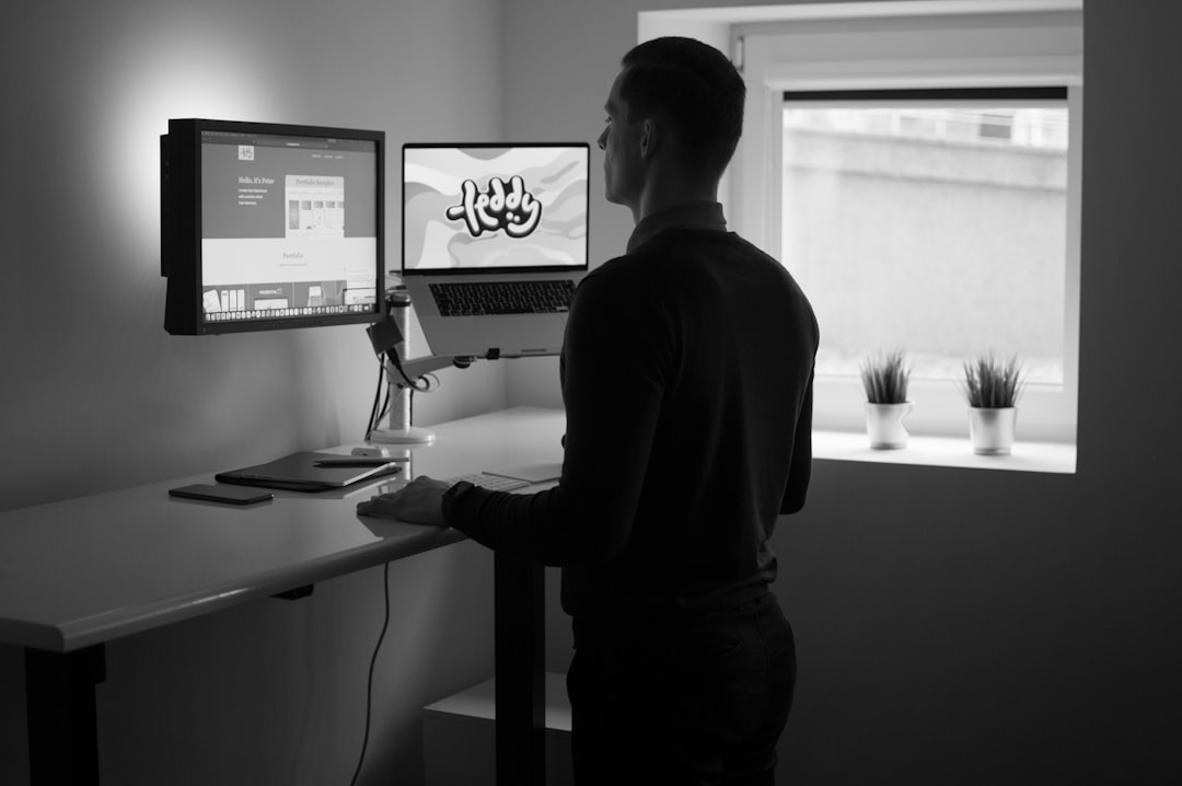 a man standing next to his dual-monitor desk