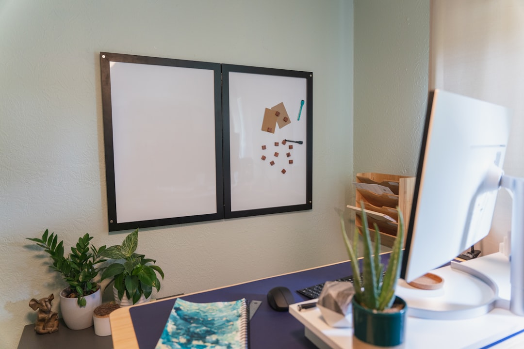 Optimize your work-from-home experience with a carefully arranged desk setup that includes plants, a notebook, and a wall-mounted whiteboard that boosts productivity.