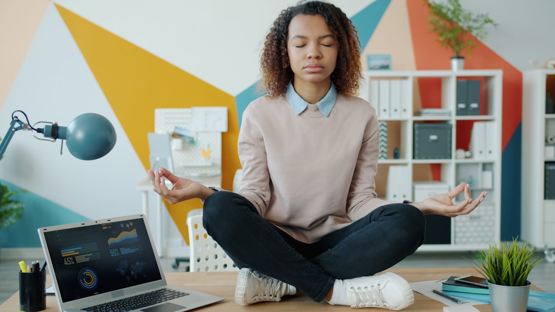 A young African American girl sits in lotus position at an office desk, enjoying relaxation and meditation. Work, stress management, and taking a break at work concept.