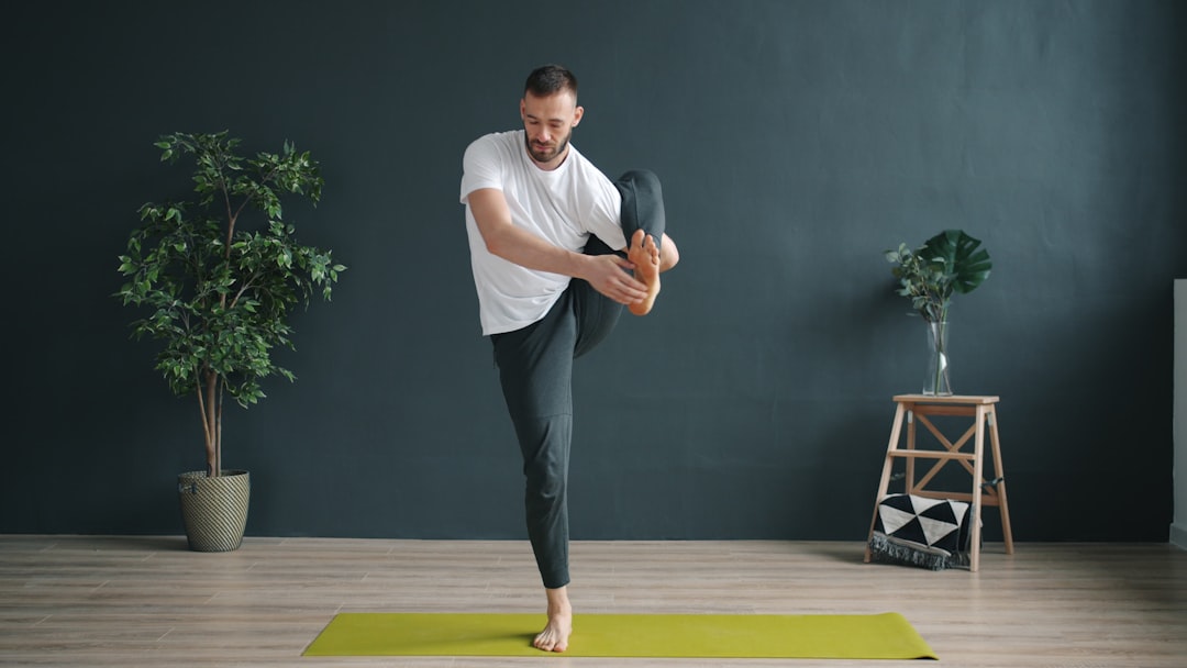 A yoga instructor, a serious bearded man, stretches his legs while balancing on one foot in a modern studio gym and demonstrates a new asana. People and sports concept.