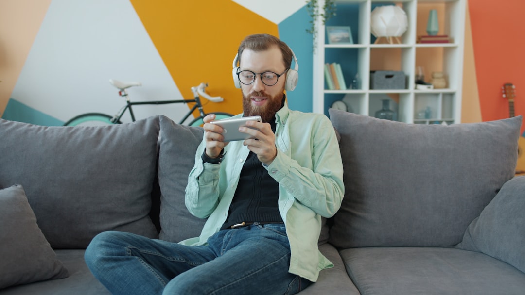 Portrait of a happy young man playing a mobile video game on a smartphone while relaxing alone on a couch at home. Youth and lifestyle concept.