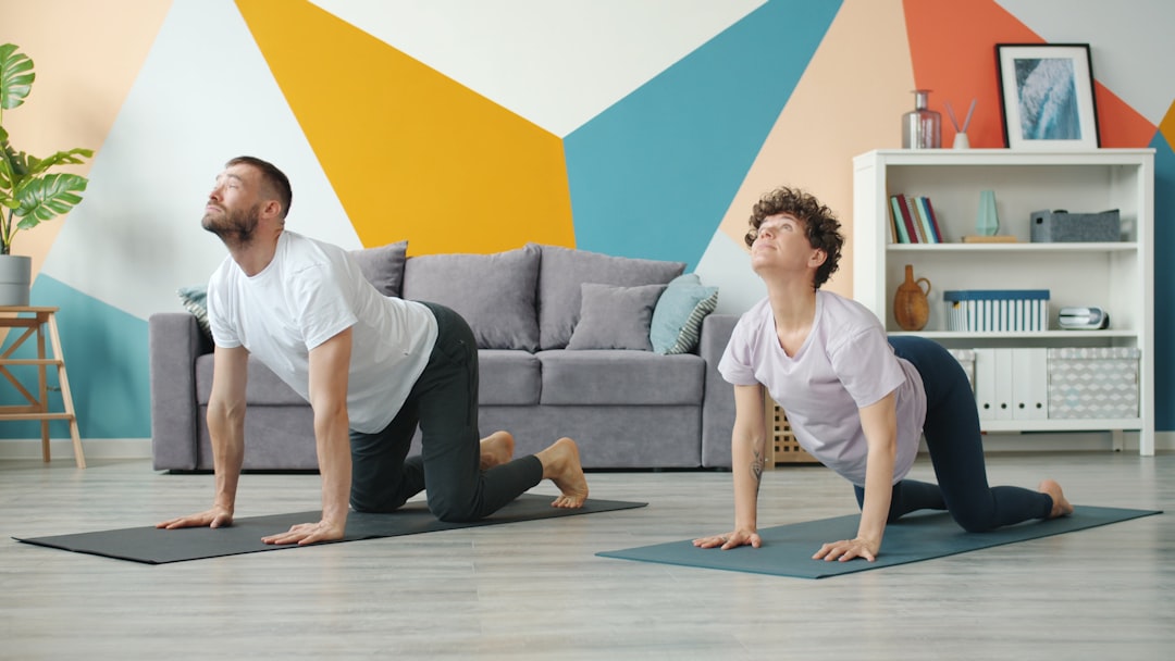 Slow-motion footage of a young, attractive married couple doing yoga together in an apartment, taking care of their health and working out their bodies. A cozy room can be seen in the background.